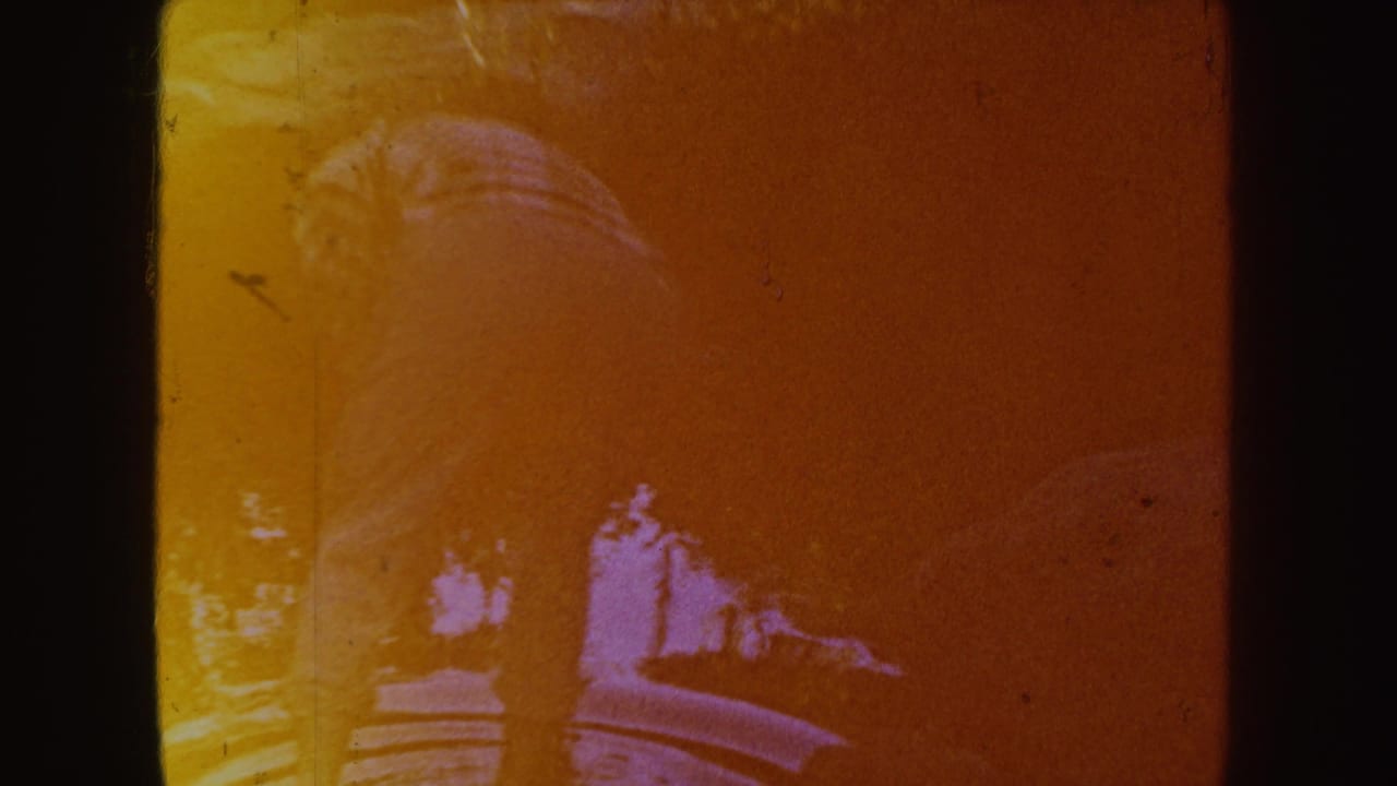 Woman bends over a shallow stream within a warm orange-tinted 8mm frame.