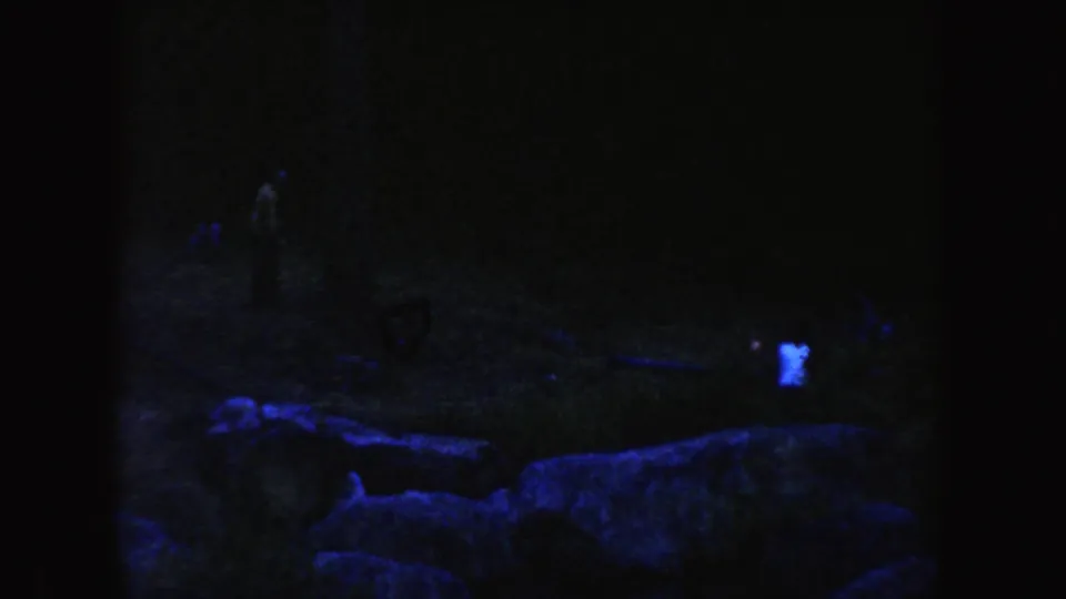1954 South Dakota 8mm frame showing a dark rocky outdoor area with faint people visible in blue-purple dusk exposure.