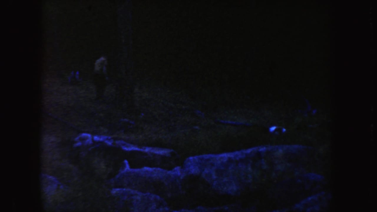1954 South Dakota home-movie frame with low rocks in front and a barely visible person in the dark landscape.