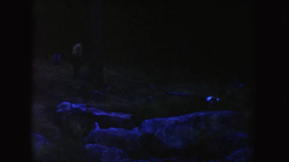 1954 South Dakota home-movie frame with low rocks in front and a barely visible person in the dark landscape.