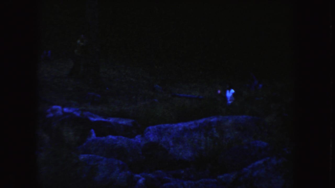 1954 South Dakota 8mm frame showing faint figures in a blue-purple dusk landscape with rocks across the foreground.