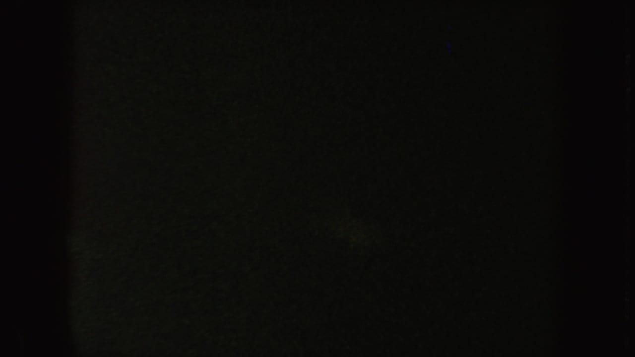 Dim 8mm frame from the South Dakota clip, largely obscured by darkness with faint green-blue surface texture.