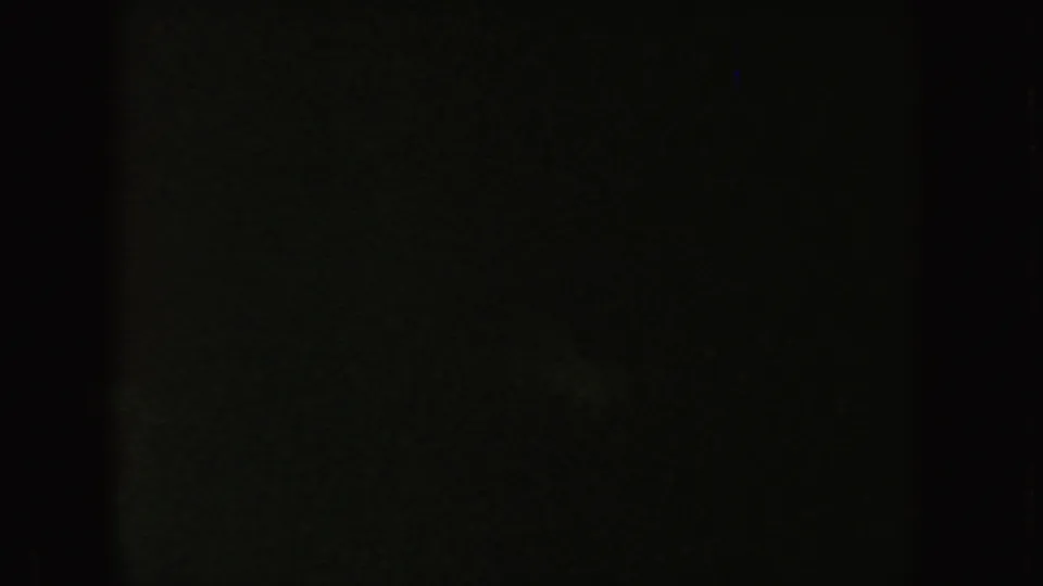 Dim 8mm frame from the South Dakota clip, largely obscured by darkness with faint green-blue surface texture.