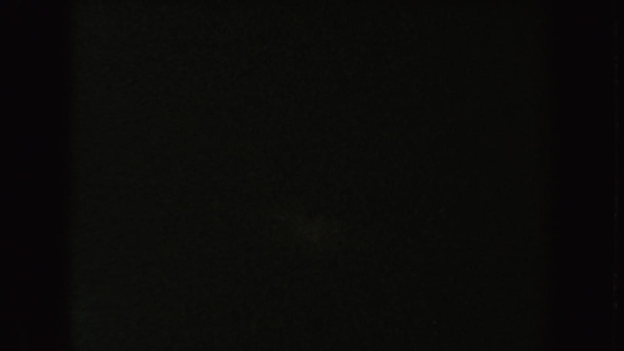 Low-exposure 1954 8mm frame with faint mottled texture and little readable detail after the visible outdoor action.