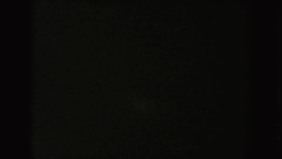 Low-exposure 1954 8mm frame with faint mottled texture and little readable detail after the visible outdoor action.