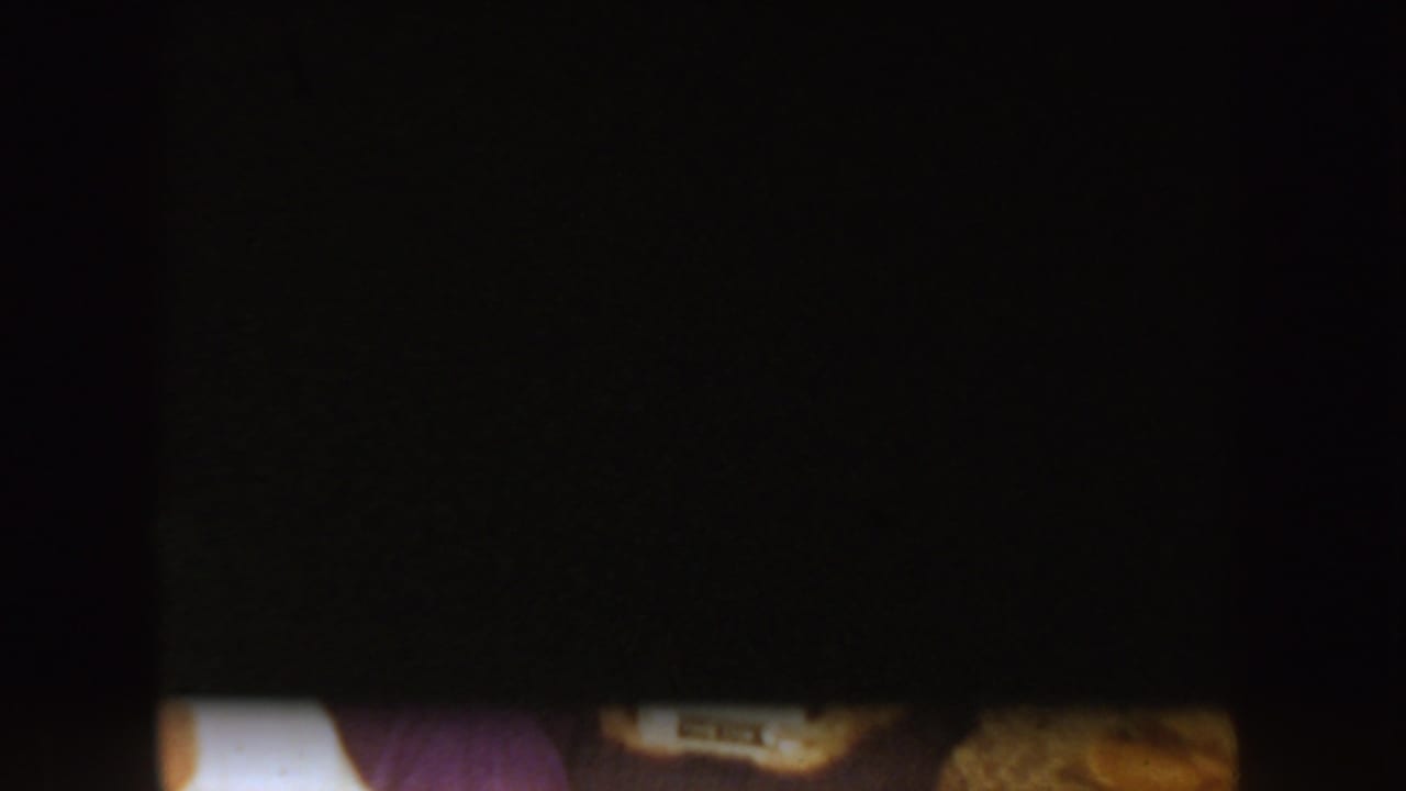 Very dark 8mm frame with a narrow bright strip and indistinct color shapes, offering minimal identifiable detail.