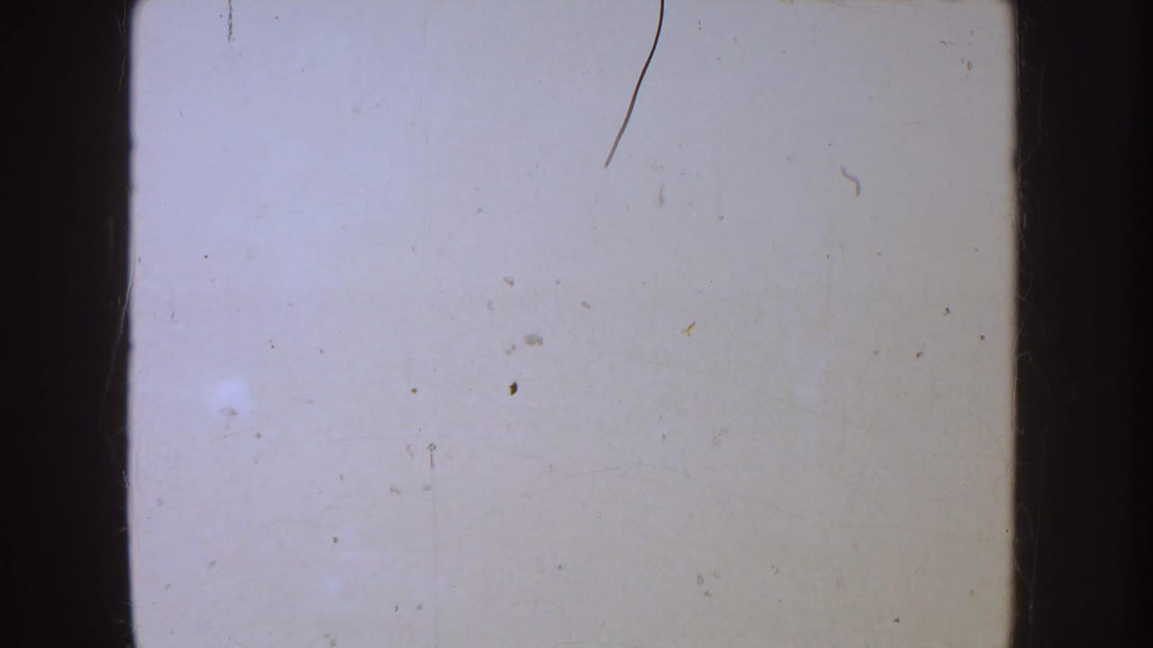 Overexposed 8mm frame with pale blank area, visible scratches, dust specks, and dark rounded film borders.