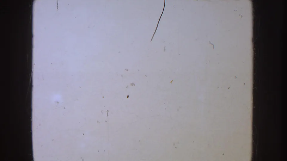 Overexposed 8mm frame with pale blank area, visible scratches, dust specks, and dark rounded film borders.