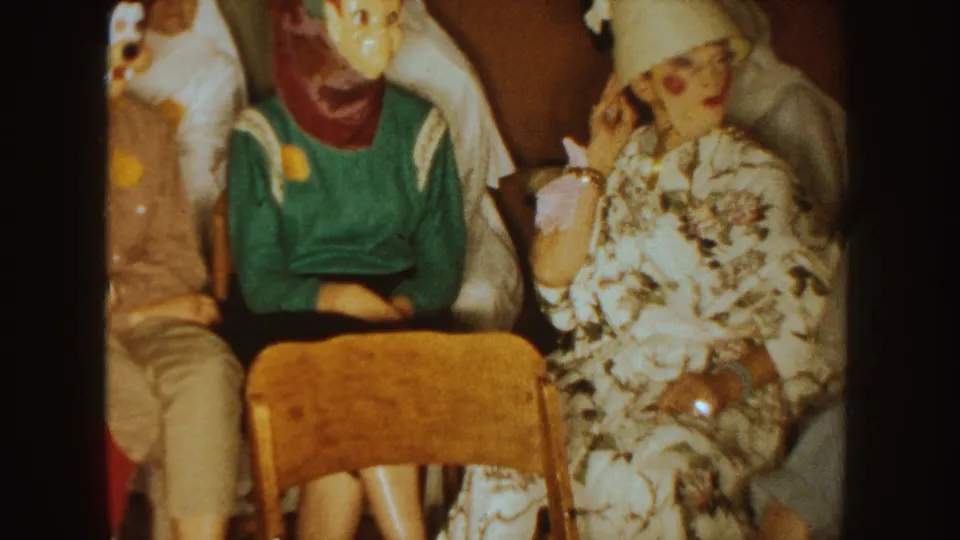 1954 South Dakota home-movie frame showing seated Halloween guests, including a floral dress and hat costume.