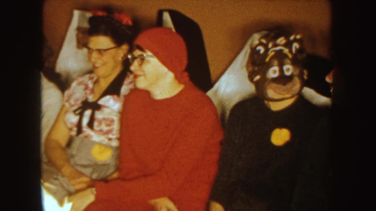 Two adults sit beside a person in a red hood and a guest wearing a black animal mask.