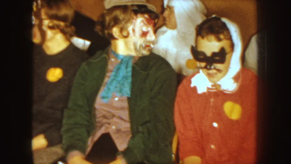 1954 South Dakota Halloween frame showing costumed guests, including face paint, a white hooded costume, and a red masked figure.