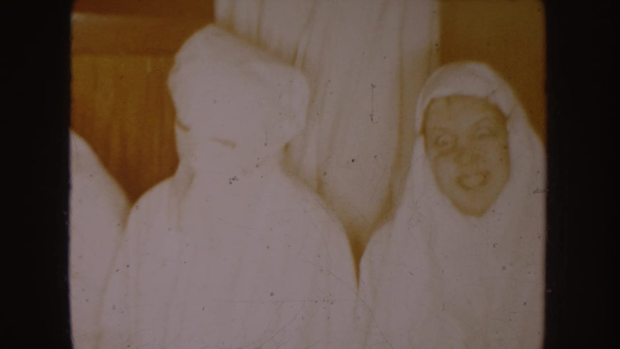 White-clad shorter figures beside a taller robed figure in a dim interior.