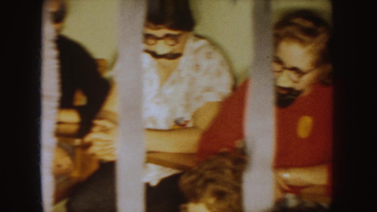 1954 South Dakota home-movie frame of students seated at desks with fake mustaches and costume glasses during a school party.