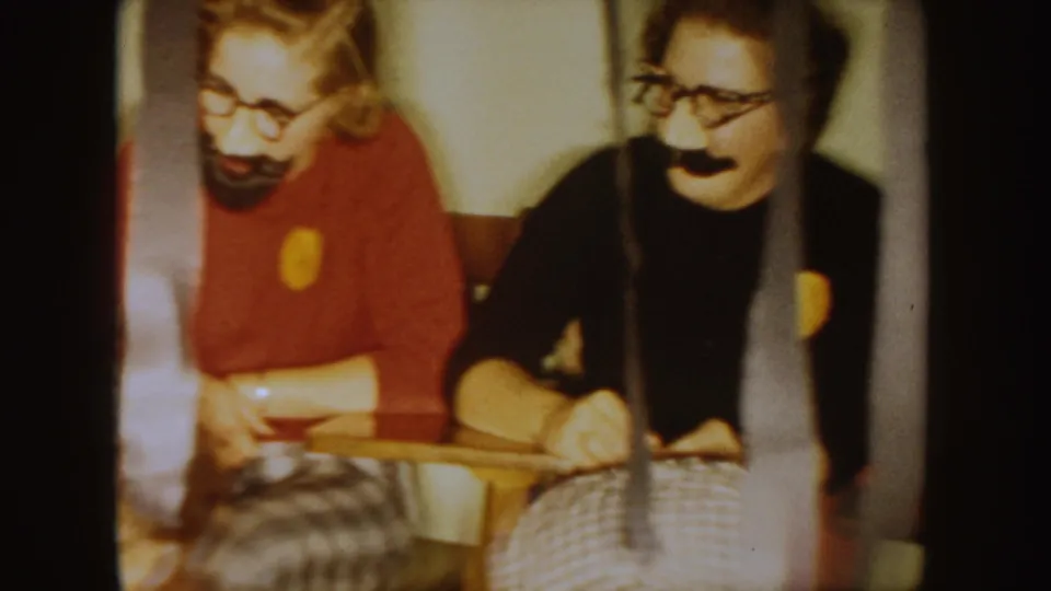 Two students wearing fake mustaches and glasses sit at a classroom desk in the 1954 South Dakota school-party footage.