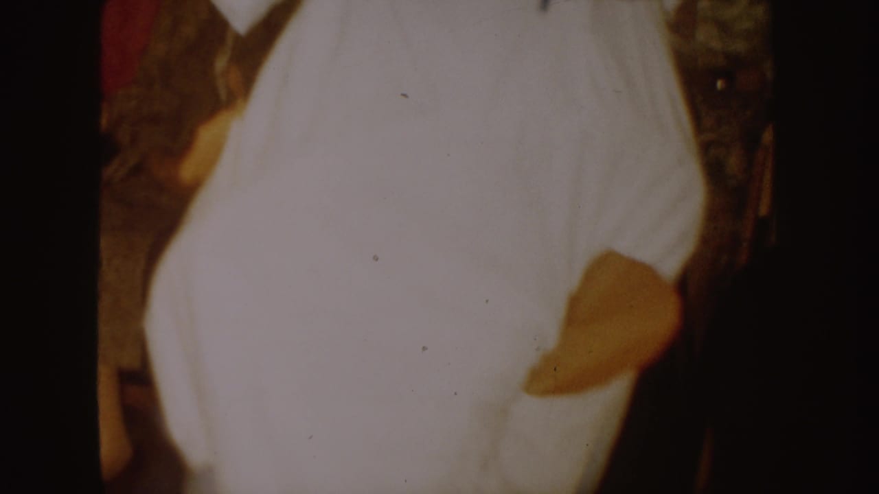 1954 South Dakota 8mm frame showing a close, soft-focus view of a white costume with a dark stain or patch indoors.