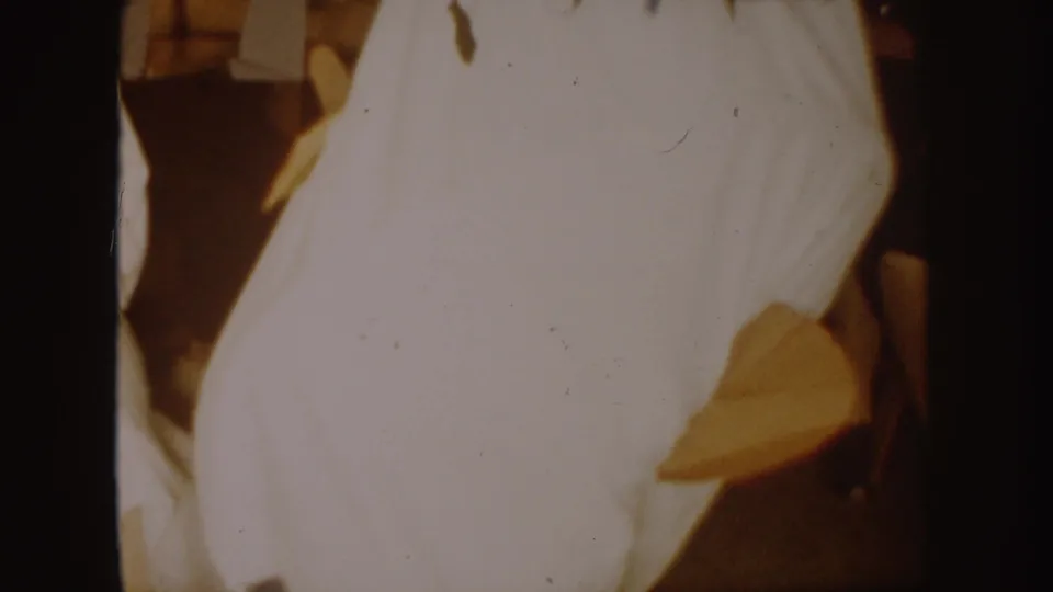 Close 8mm view of the white costume in motion, with a dark area near the side and indoor background detail.