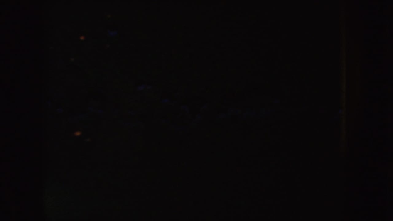 Dark 1954 8mm South Dakota frame with faint orange specks, heavy grain, and indistinct interior shapes.