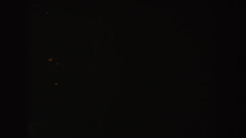 Dark South Dakota 8mm frame showing dense shadow, scattered warm specks, and no identifiable people or objects.