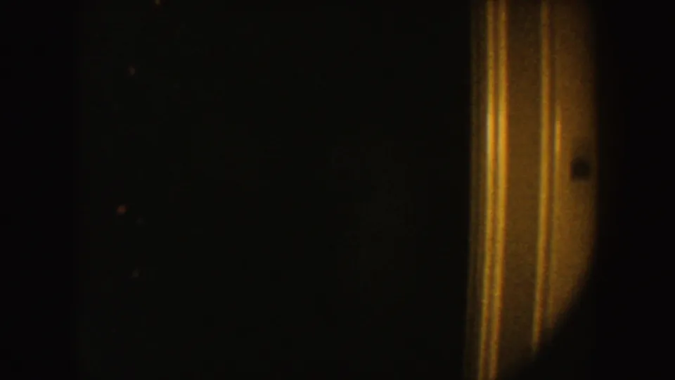 Low-light 8mm frame with warm vertical edge streaks, dark surrounding space, and visible film grain.