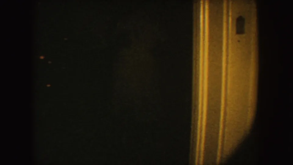 1954 South Dakota 8mm frame showing a tan doorway jamb with a small gray switch plate in dim warm light.