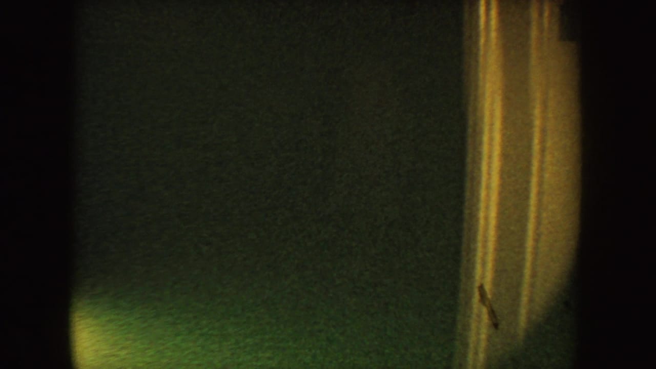 1954 South Dakota home-movie frame with tan door trim, dark interior space, and a faintly visible wall surface.