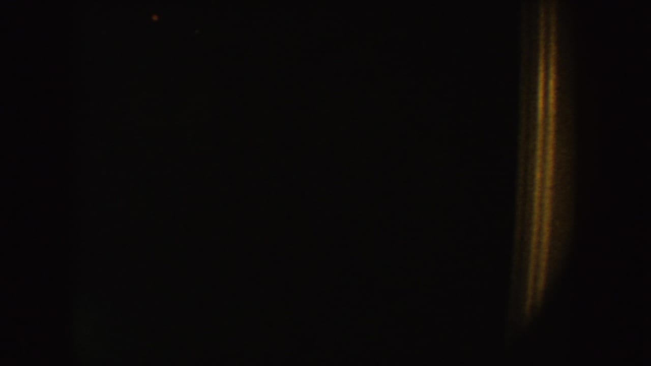 Underexposed 1954 South Dakota 8mm frame showing a dark interior and a narrow warm light band near the right side.