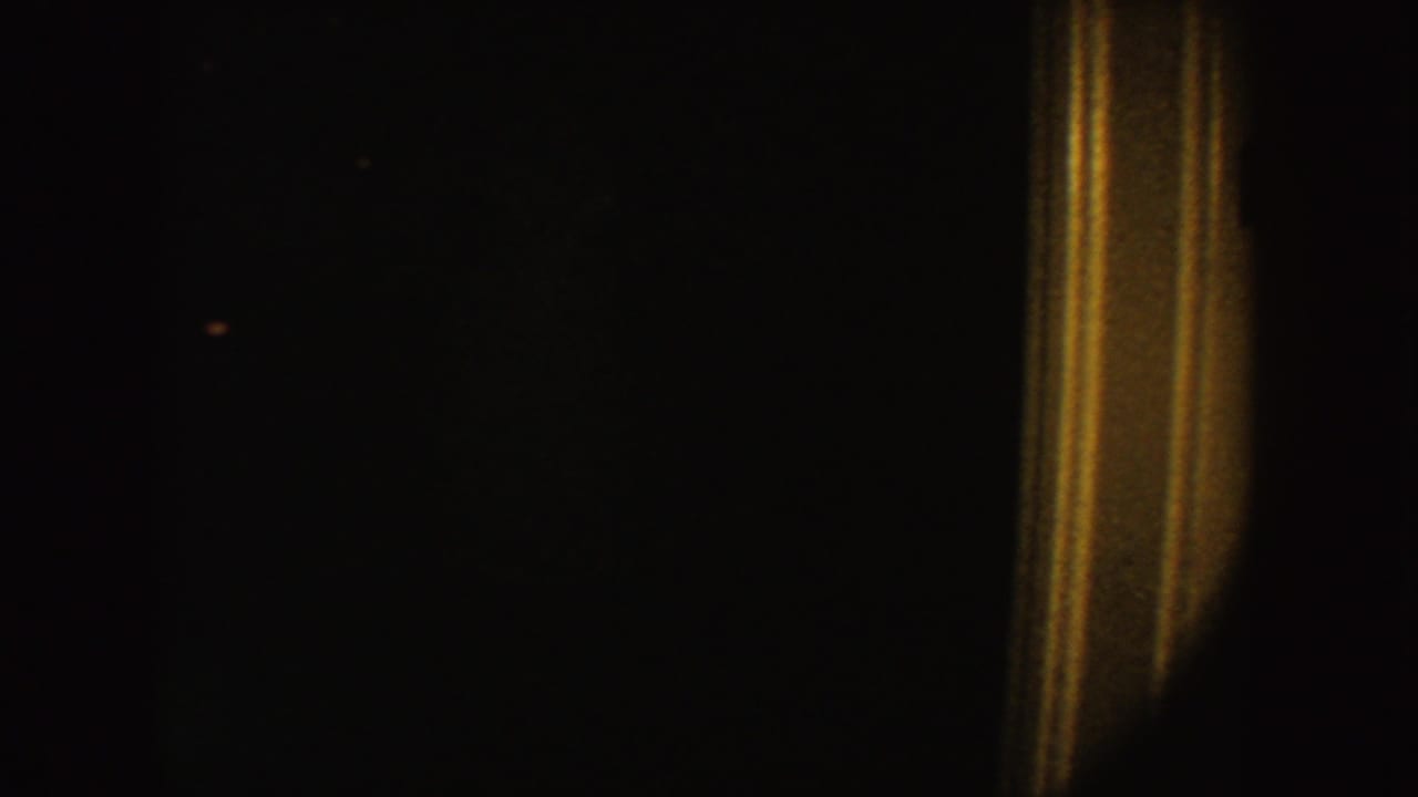 Underexposed 1954 South Dakota 8mm frame with a warm vertical light streak against a nearly black interior.