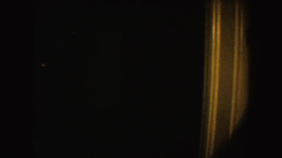 Underexposed 1954 South Dakota 8mm frame with a warm vertical light streak against a nearly black interior.