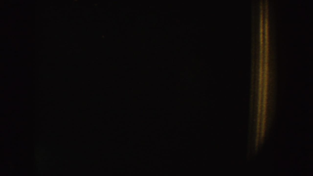 1954 South Dakota 8mm frame showing a dim interior, warm vertical glow, and faint rectangular dark areas.