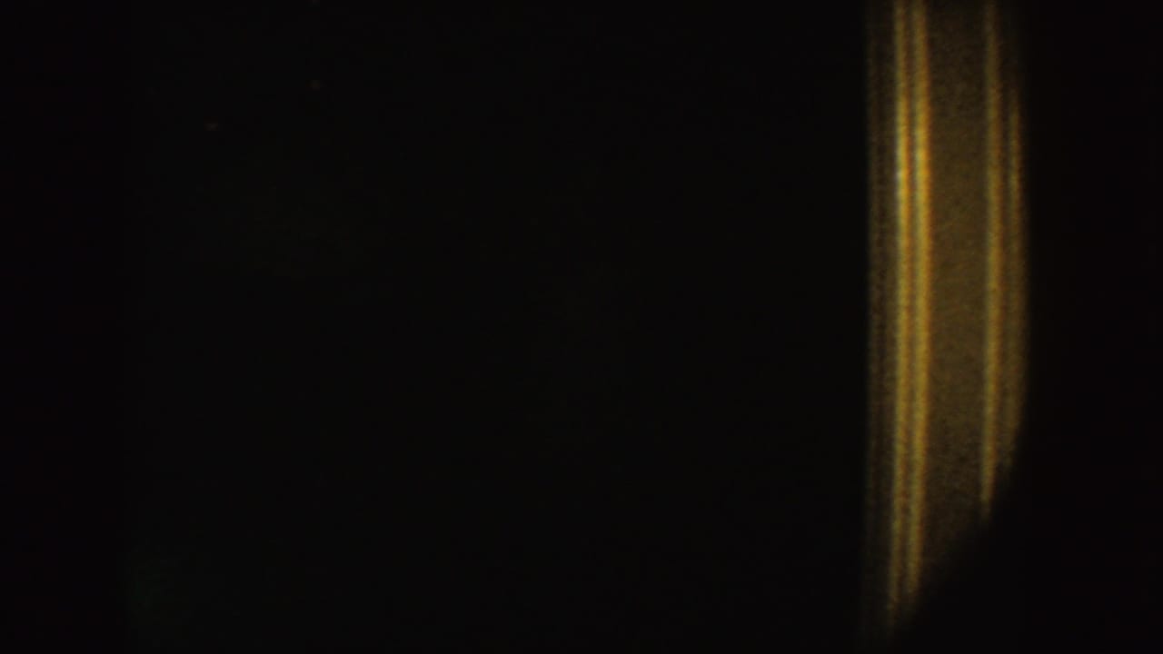 Underexposed 1954 South Dakota home-movie frame with a warm door-like light strip in a dark interior.