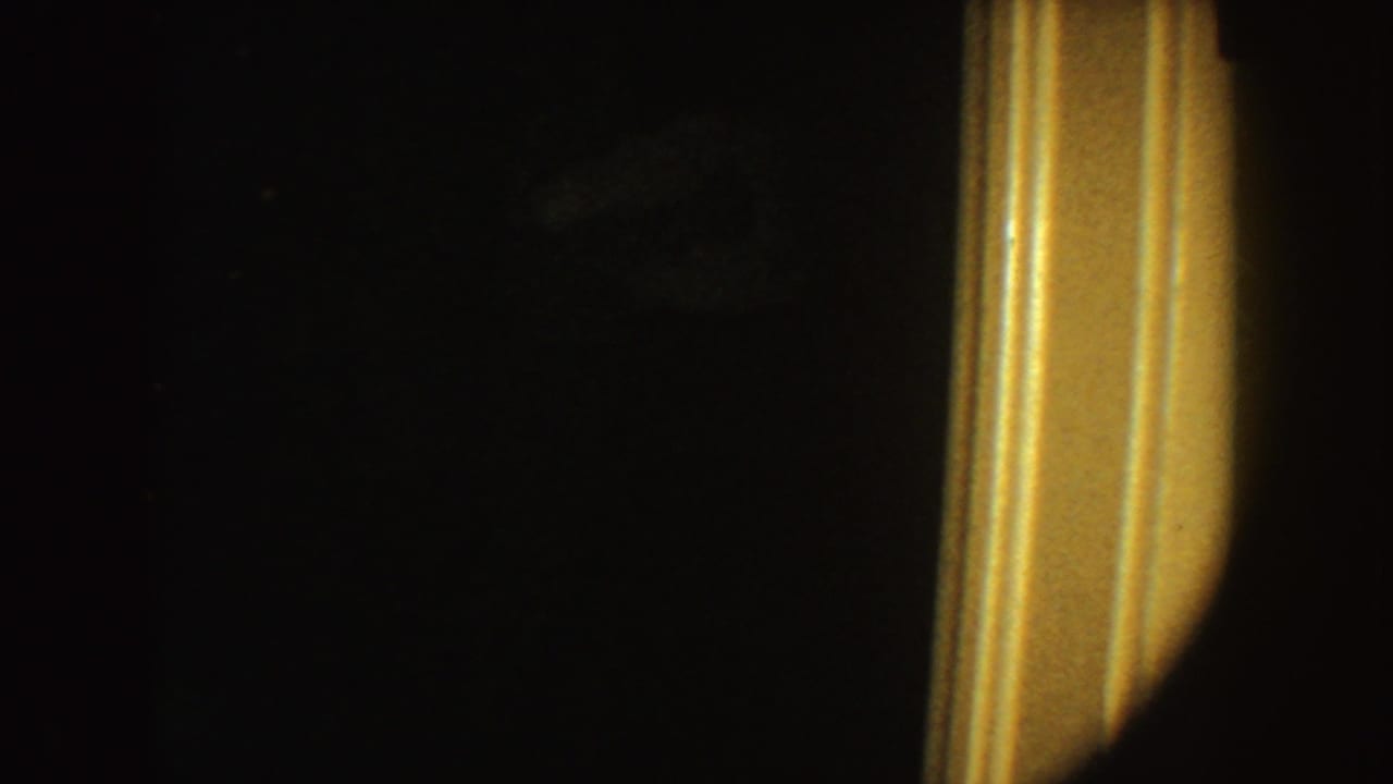 1954 South Dakota 8mm frame with a mostly black room and a warm vertical light source at the right edge, possibly a doorway or lamp.