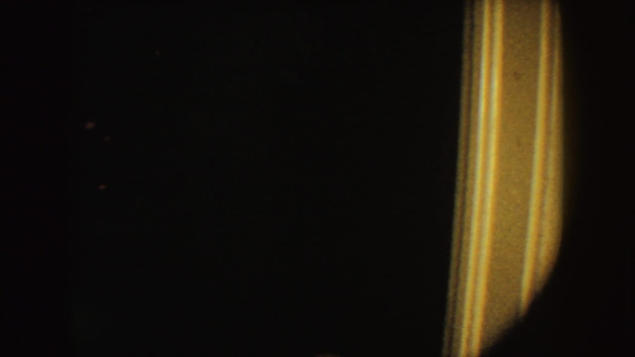 Underexposed 1954 South Dakota 8mm frame showing a warm vertical light strip and adjacent dark silhouette in a dim interior.