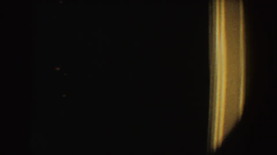 1954 South Dakota 8mm frame showing a nearly black low-light scene with a narrow warm light and indistinct shadowed forms.