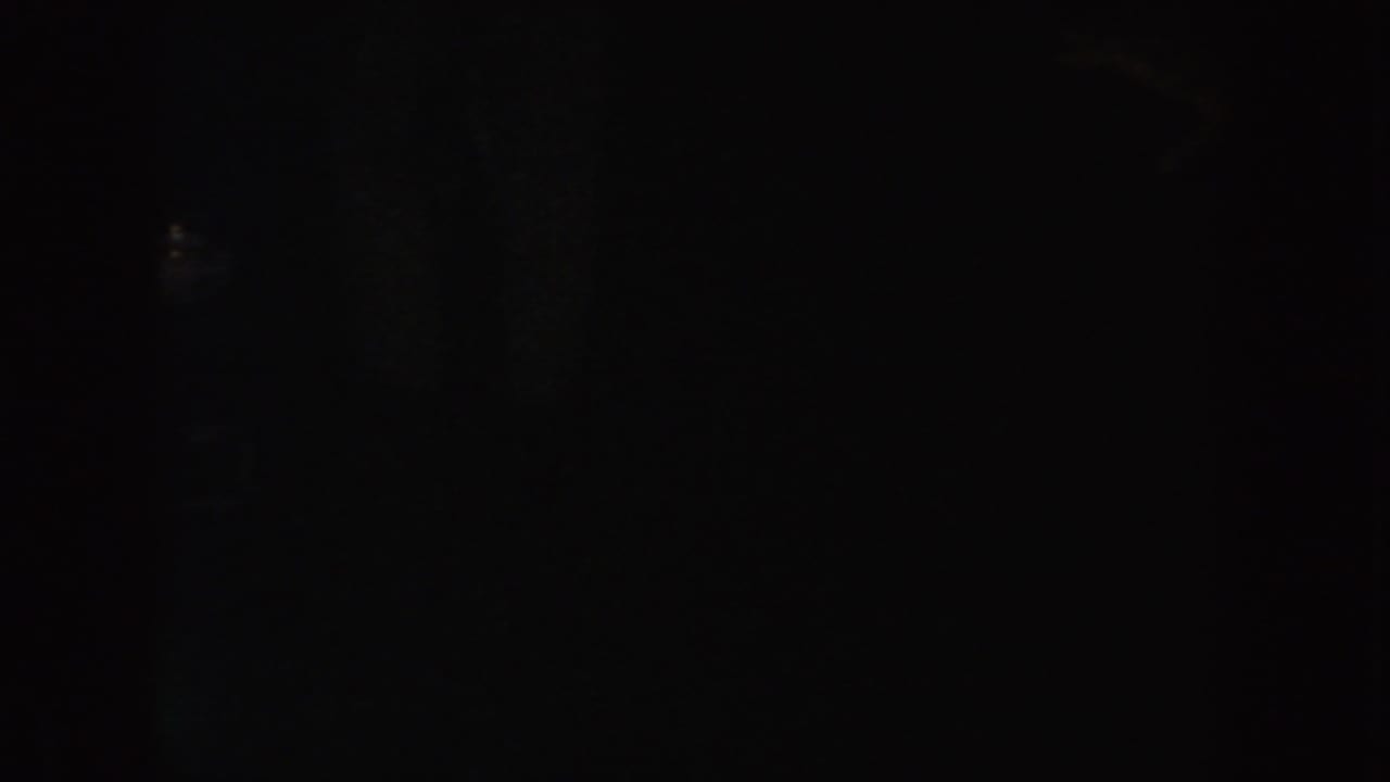 Low-exposure 8mm frame from 1954 South Dakota with possible passing legs or figures near a warm vertical light source.