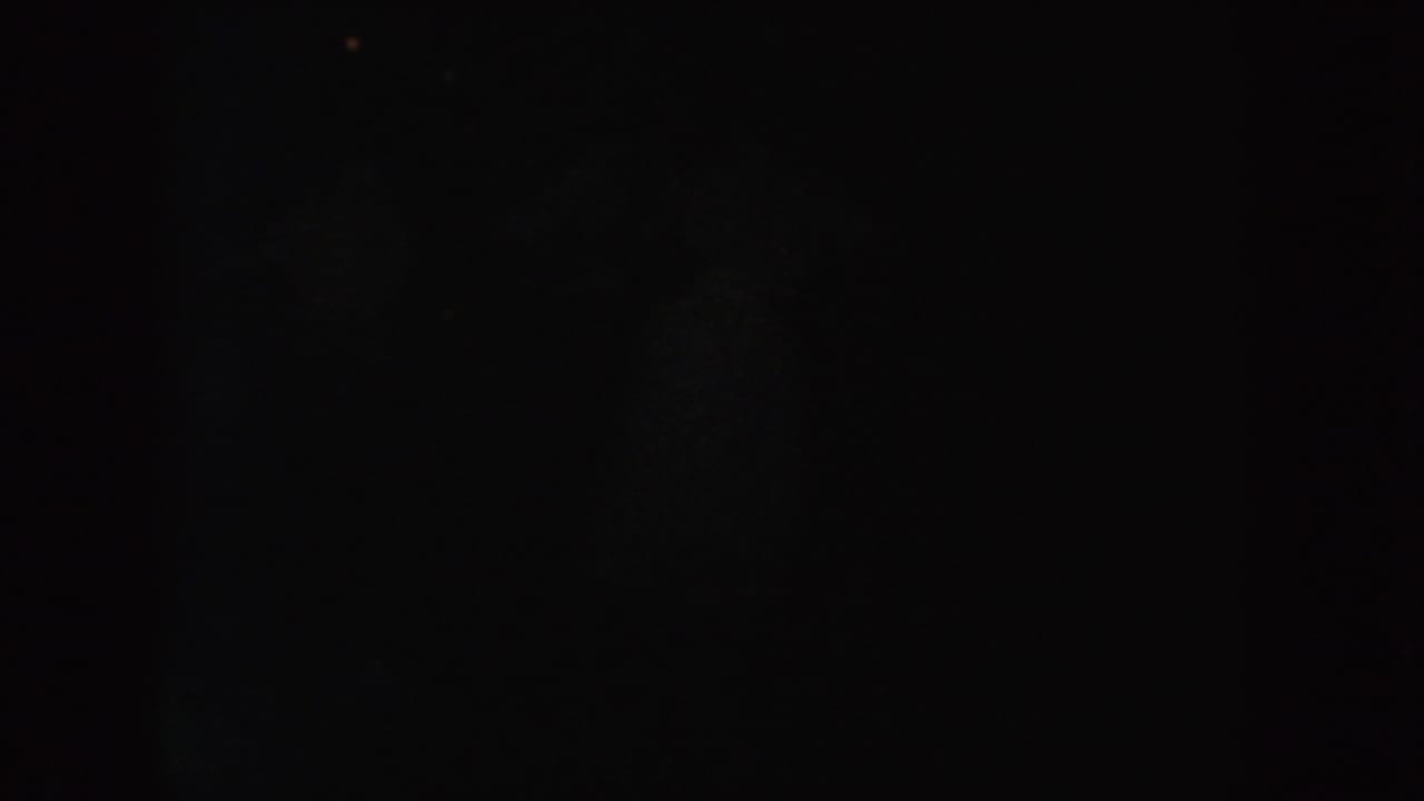 Dark 1954 South Dakota 8mm frame with faint scattered light points, heavy grain, and no identifiable people or setting.
