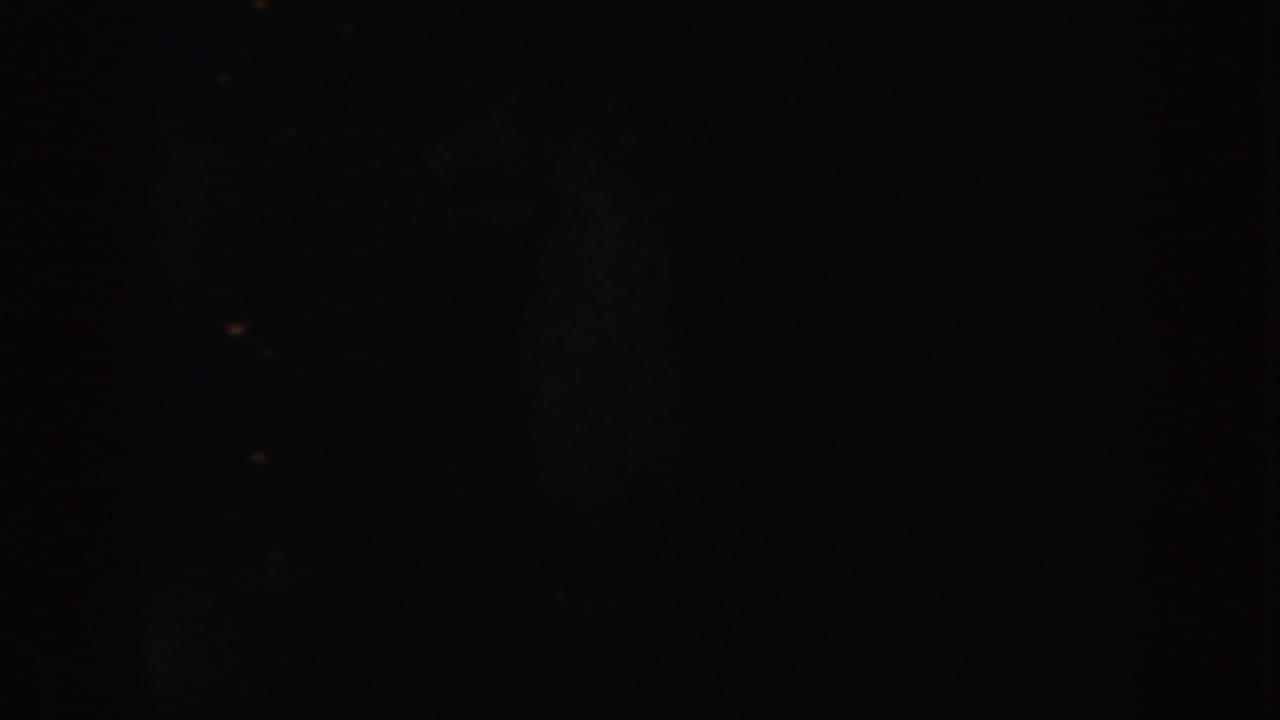 Very low-light 1954 South Dakota home-movie frame showing indistinct vertical darkness, grain, and faint points of light.