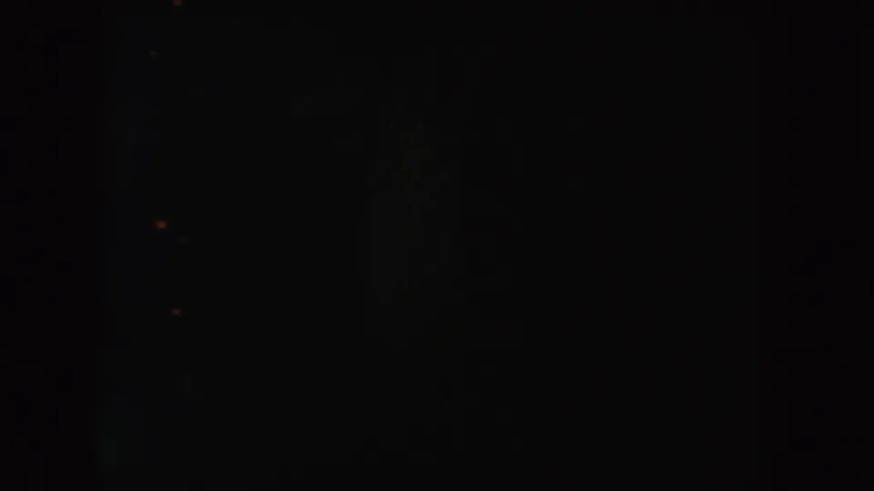 Very low-light 1954 South Dakota home-movie frame showing indistinct vertical darkness, grain, and faint points of light.
