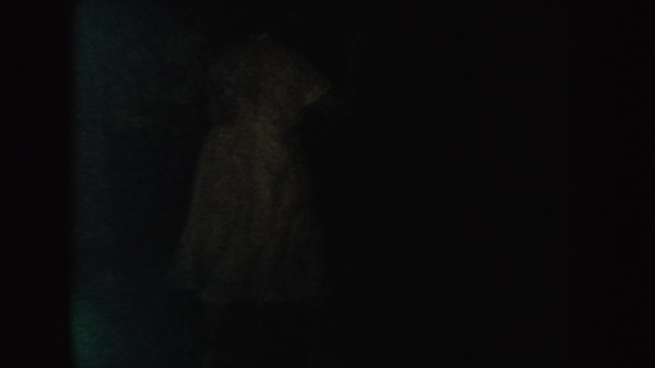 A faint figure-like form in a pale garment appears in a dark 1954 South Dakota 8mm frame, with facial detail obscured.