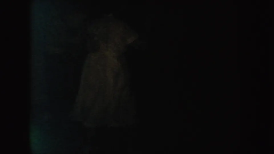 A faint figure-like form in a pale garment appears in a dark 1954 South Dakota 8mm frame, with facial detail obscured.