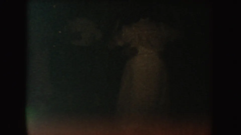 A dim side view of a person in a light garment crosses a dark 1954 South Dakota 8mm home-movie frame.