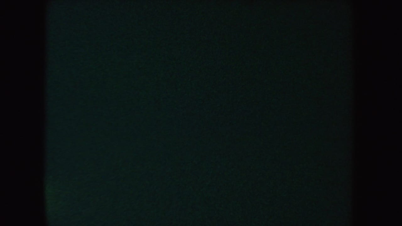 An underexposed 8mm frame from the 1954 South Dakota clip, showing mostly dark film with a faint green cast and black vertical borders.