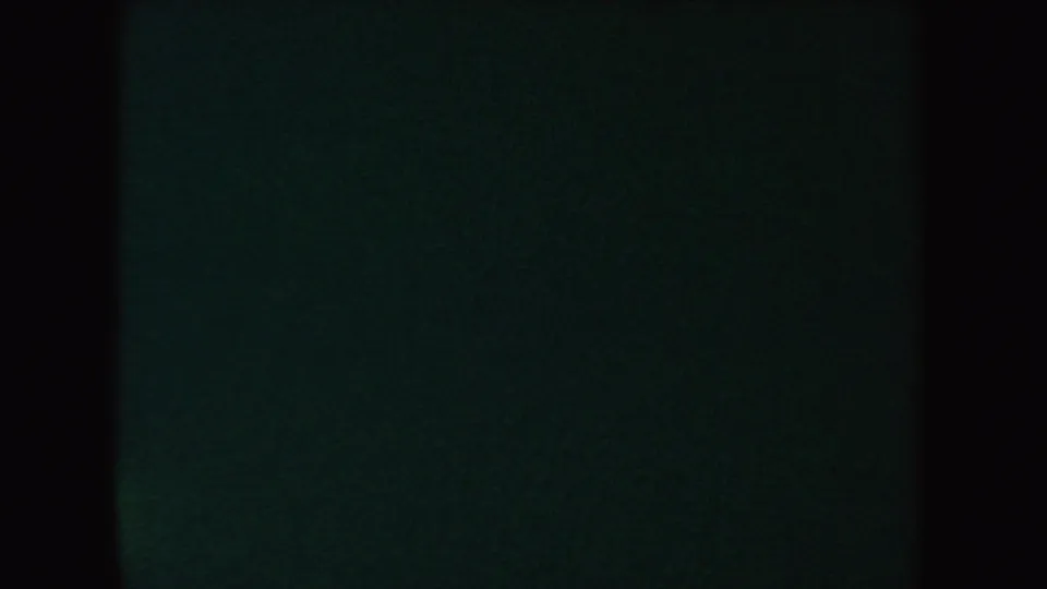 An underexposed 8mm frame from the 1954 South Dakota clip, showing mostly dark film with a faint green cast and black vertical borders.