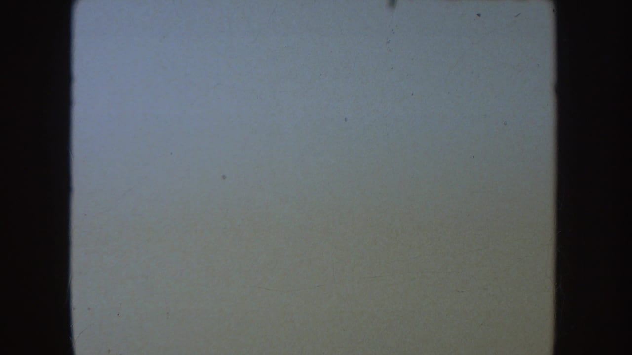 A pale, nearly blank 8mm frame with dark side borders, dust specks, and soft fading in the 1954 South Dakota home movie.