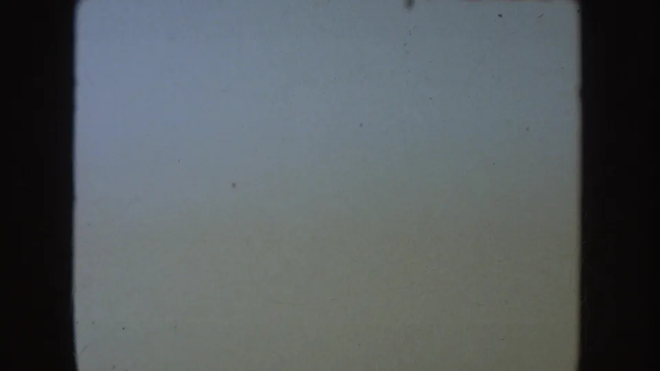 A pale, nearly blank 8mm frame with dark side borders, dust specks, and soft fading in the 1954 South Dakota home movie.