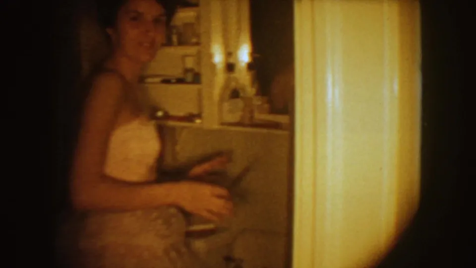 The bride smiles toward the camera while standing beside a bathroom doorway, with shelves and fixtures visible behind her.