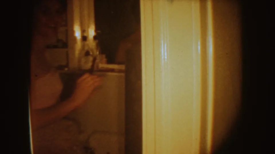The bride is partially visible near a bright door frame, with the bathroom sink area and candles dimly seen in the background.