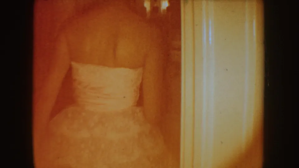 1954 South Dakota 8mm frame showing a white formal gown in a warm, soft-focused bathroom or doorway view.