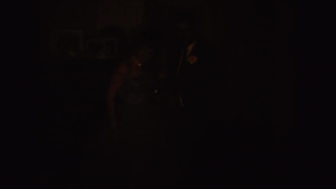 Very dark 8mm frame with faint figures and interior shapes barely visible.