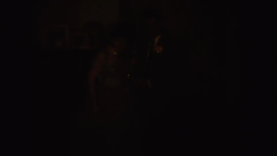 Dark, underexposed 1954 8mm home-movie frame from South Dakota with faint figures and household shapes barely visible.