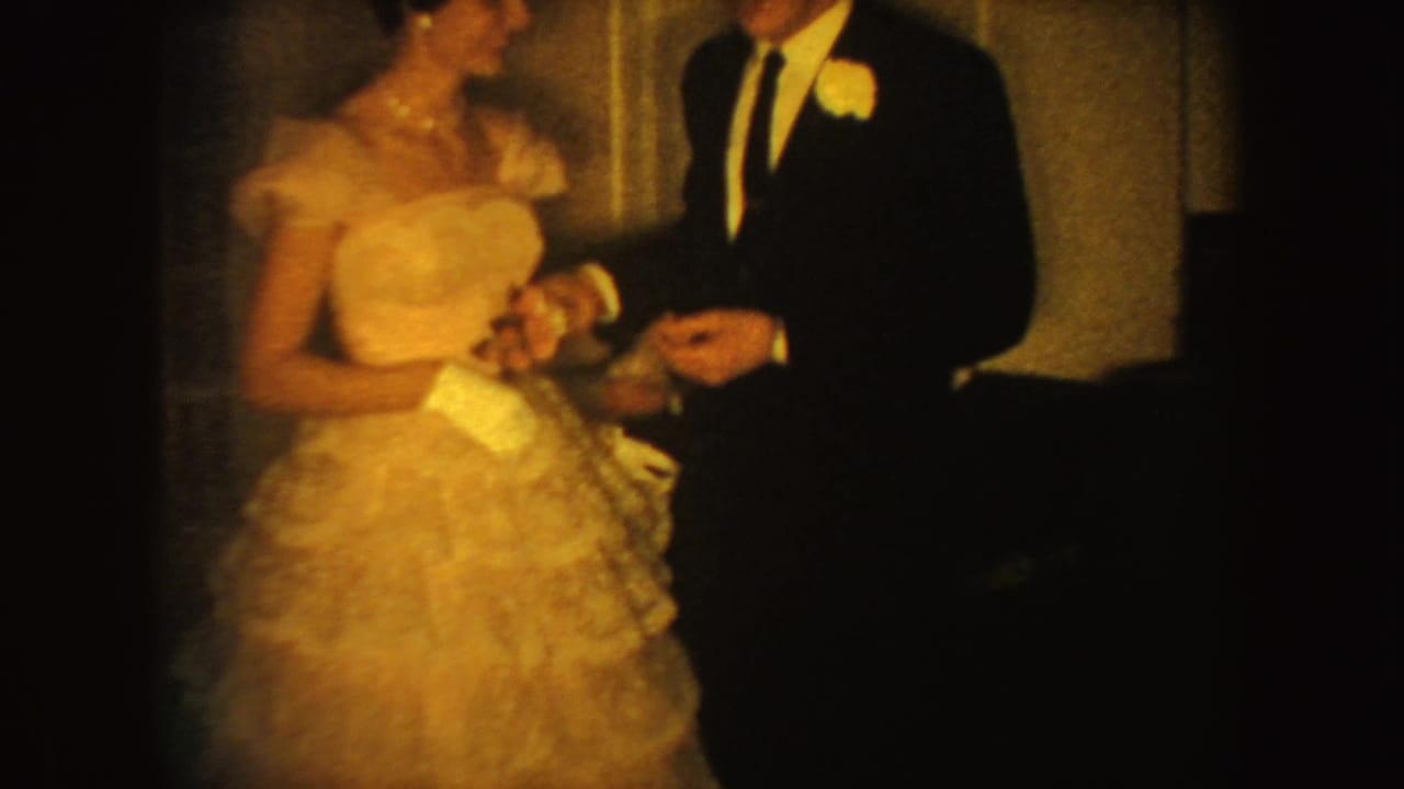 In 1954 South Dakota home-movie footage, a formally dressed woman with gloves stands near a man wearing a boutonniere.
